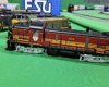 Locomotive with maroon sides with yellow stripes and black roof and top surfaces, silver trucks.
