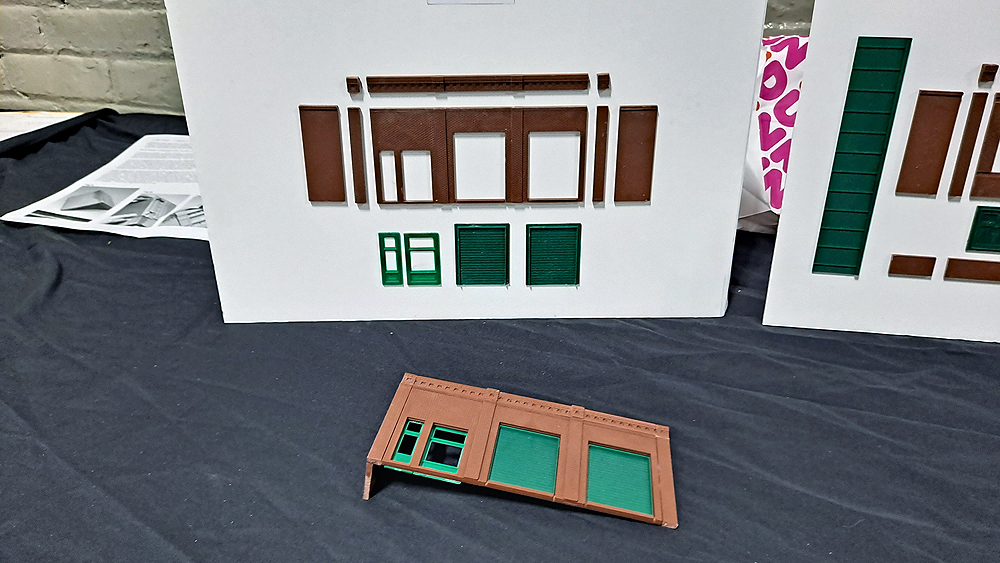 Structure walls and doors are mounted to a white board, with the assembled parts laying in front of the board on a table.