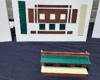 Structure walls and doors are mounted to a white board, with the assembled parts laying in front of the board on a table.