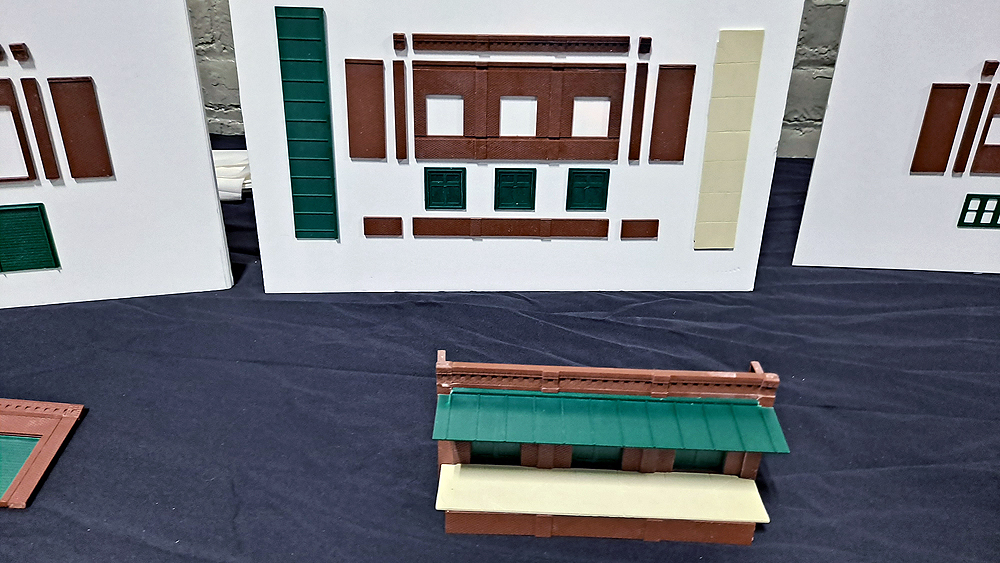 Structure walls and doors are mounted to a white board, with the assembled parts laying in front of the board on a table.