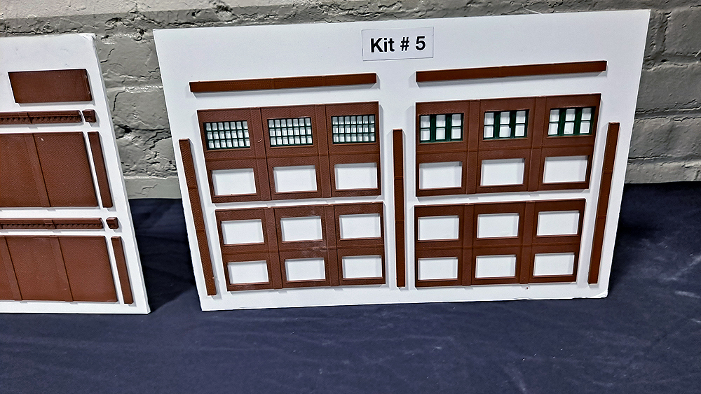 Structure walls and doors are mounted to a white board, with the assembled parts laying in front of the board on a table.