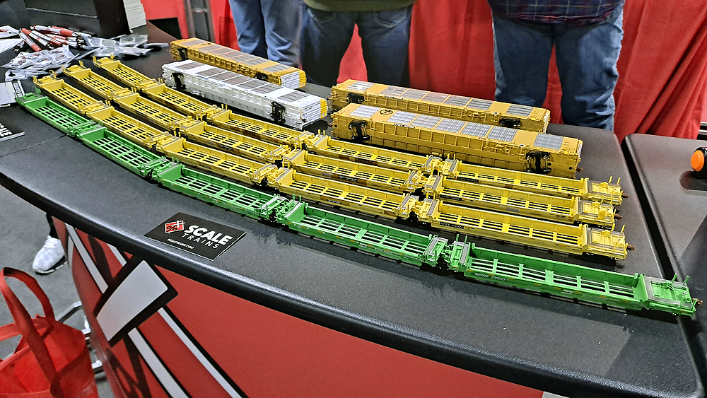 One row of green five-unit well cars sits in front of three rows of yellow five-unit well cars and for enclosed auto racks, three yellow and one white.