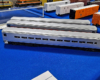 Three silver passenger coaches on blue tablecloth with white and orange mechanical refrigerator cars in the background.