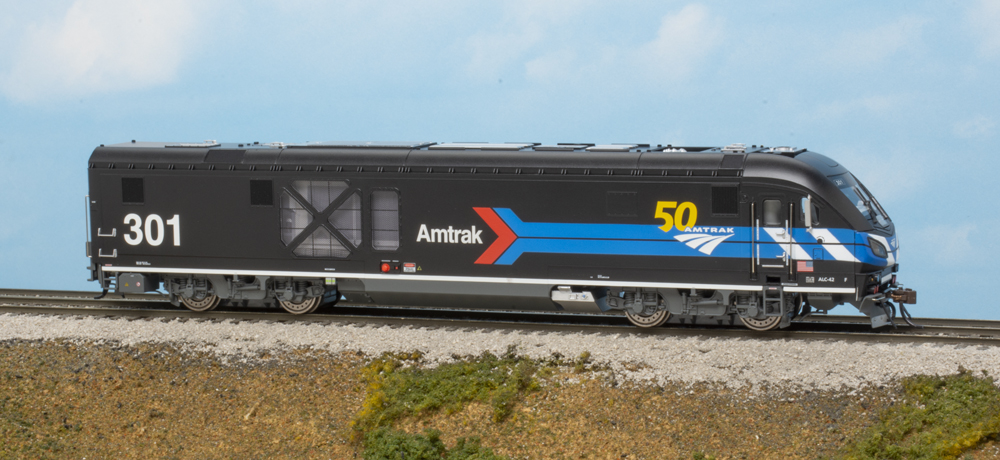 Black and gray diesel locomotive with red, white, and blue stripes on scenicked base with clouds in background.