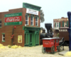 Scene on model railroad with horse-drawn wagon, steam locomotive, and 1890s-style buildings.