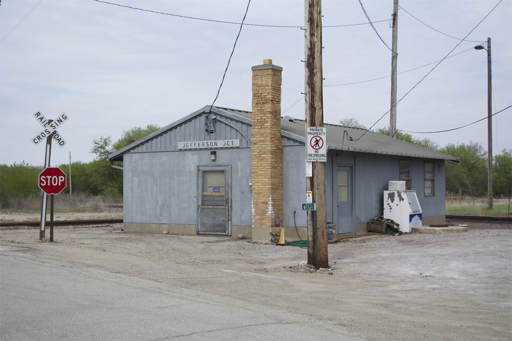 A gray metal railroad station with a brick chimney and utility pole in foreground.