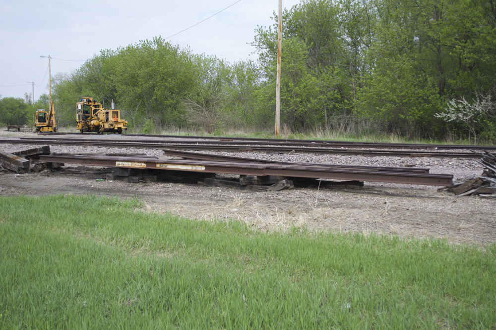 Lengths of rail on crossties. Two pieces of track equipment, painted yellow, are visible in the background.