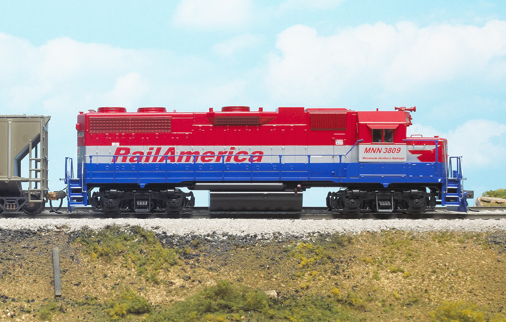 Photo of HO scale EMD hood unit painted red, silver, and blue on scenicked base with cloudy background.