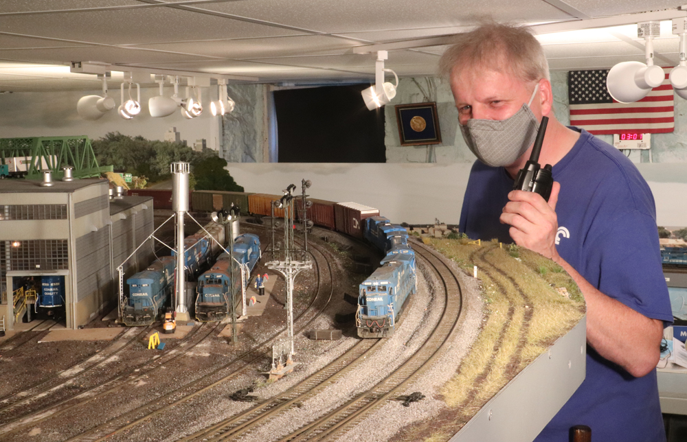 Man with mask operating a model railroad