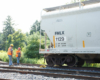 Two men in safety vests examine rerailed covered hopper