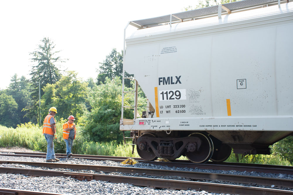 Two men in safety vests examine rerailed covered hopper