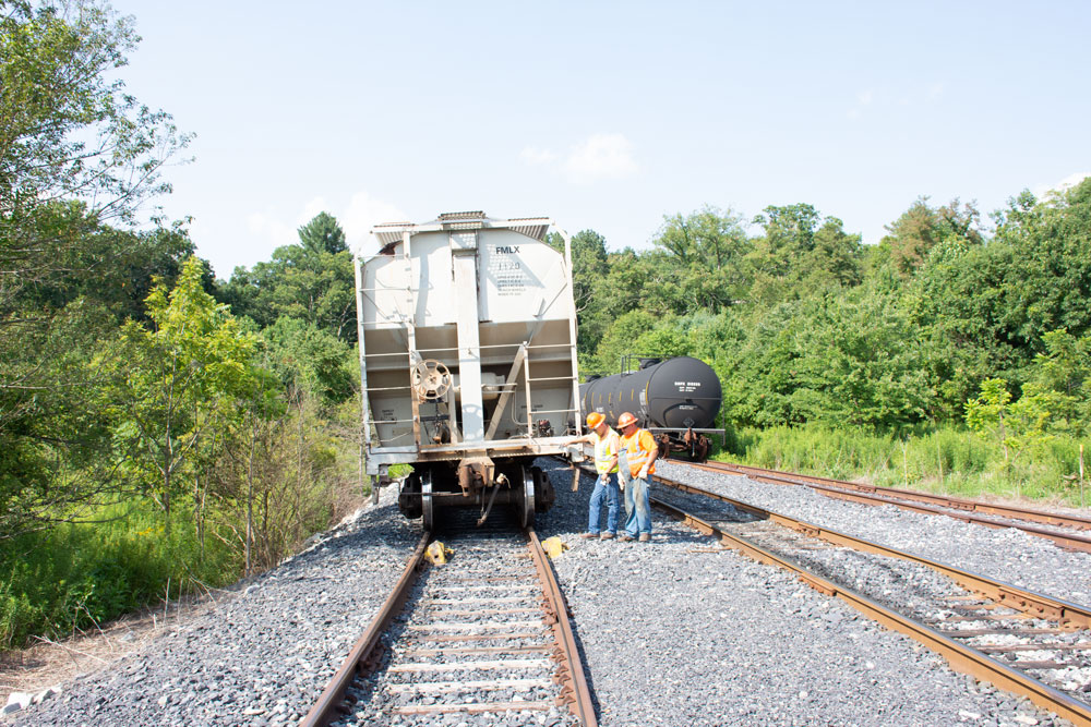 Two men in safety vests examine rerailed covered hopper