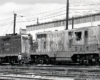 black and white photo of two locomotives couple on tracks next to building and a man with hard hat walking