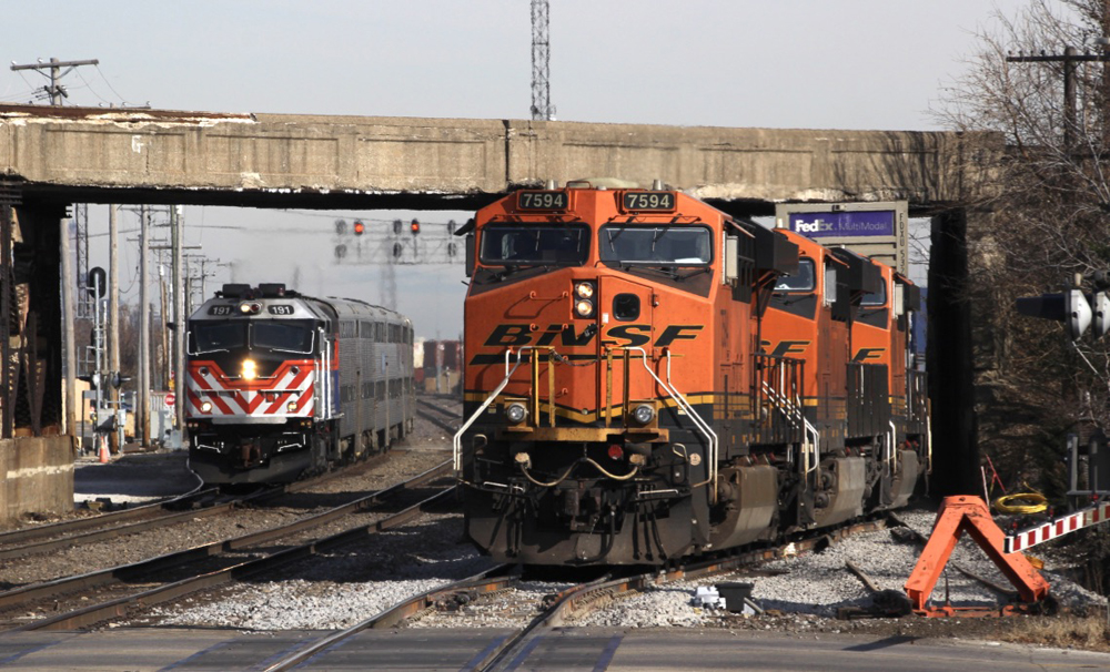 Freight train with orange locomotives leaves yard as commuter train approaches