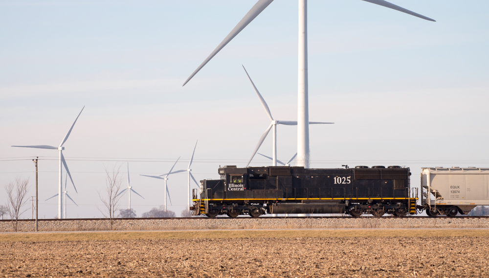 Black locomotive passes wind turbines
