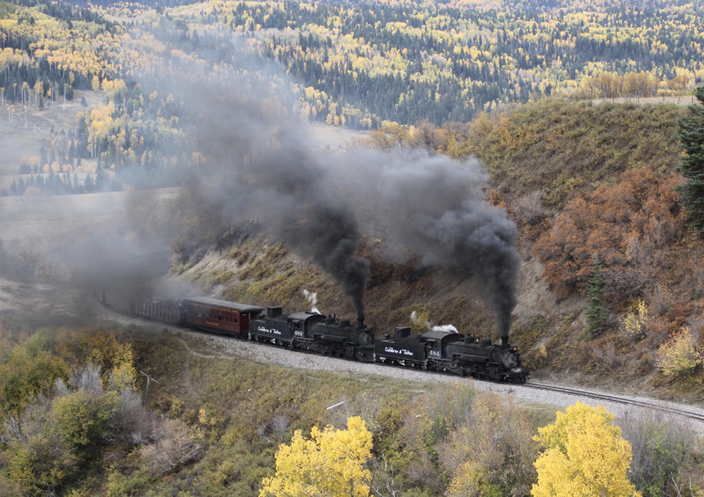 Two steam locomotives leading train through fall colors