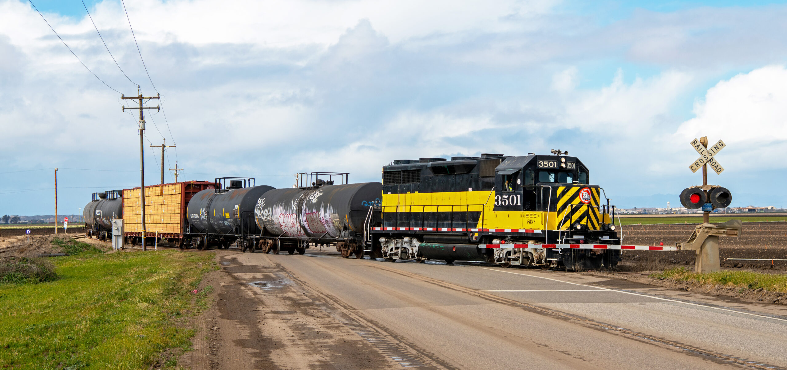 Black and yellow diesel with a few freight cars at grade crossing