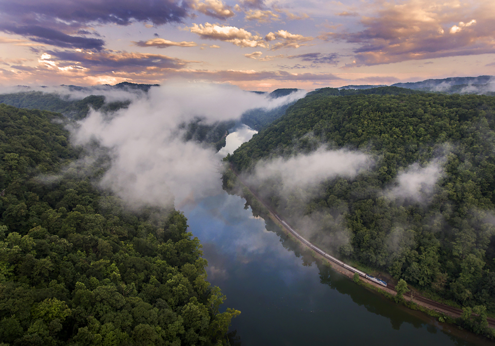 Aerial photo of passenger train in river canyon under sky of broken clouds