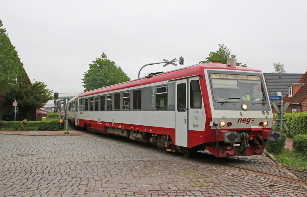Red and white DMU trainset crosses cobblestone street