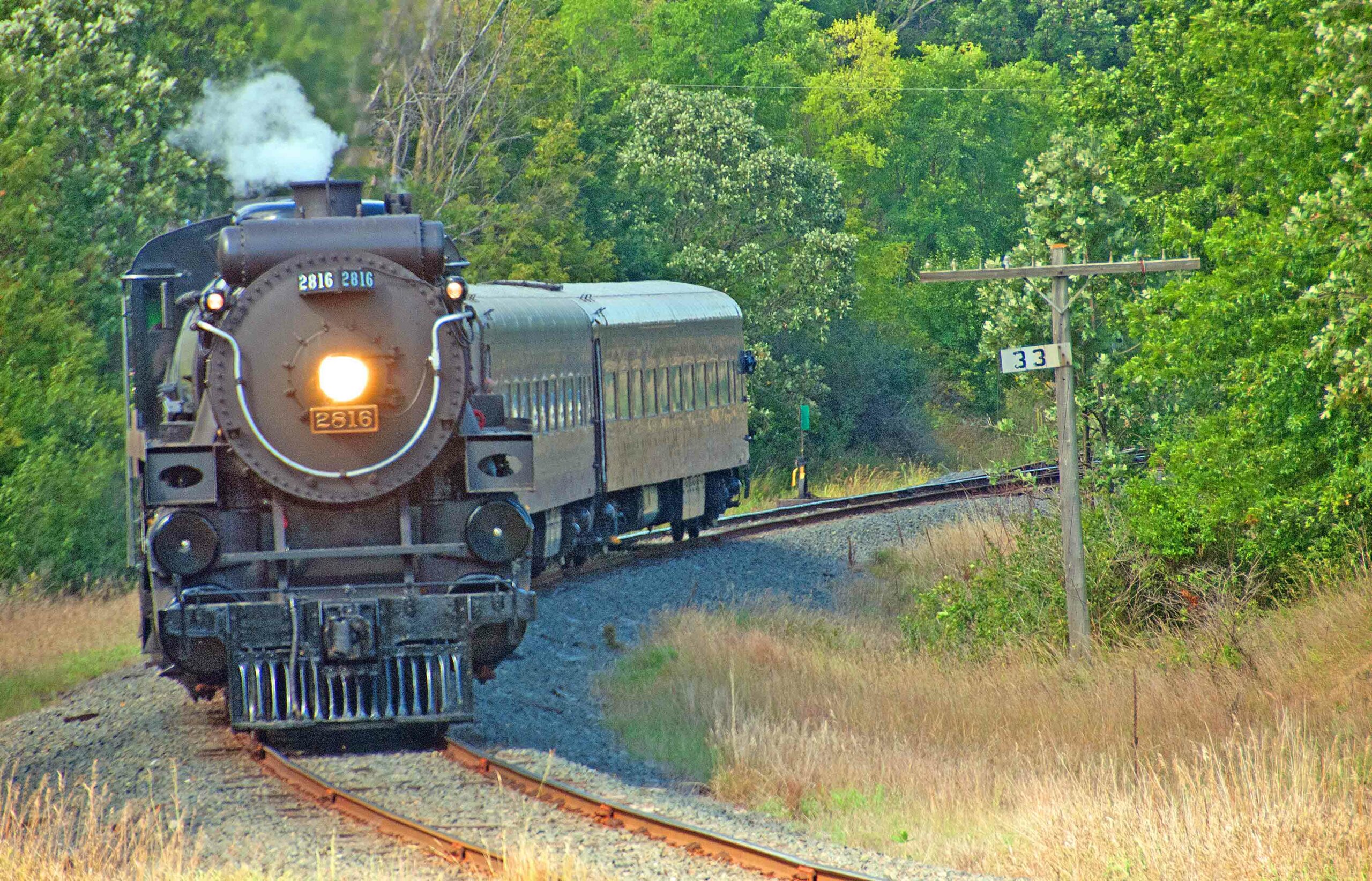 Steam locomotive with short passenger train in low angle sunlight.