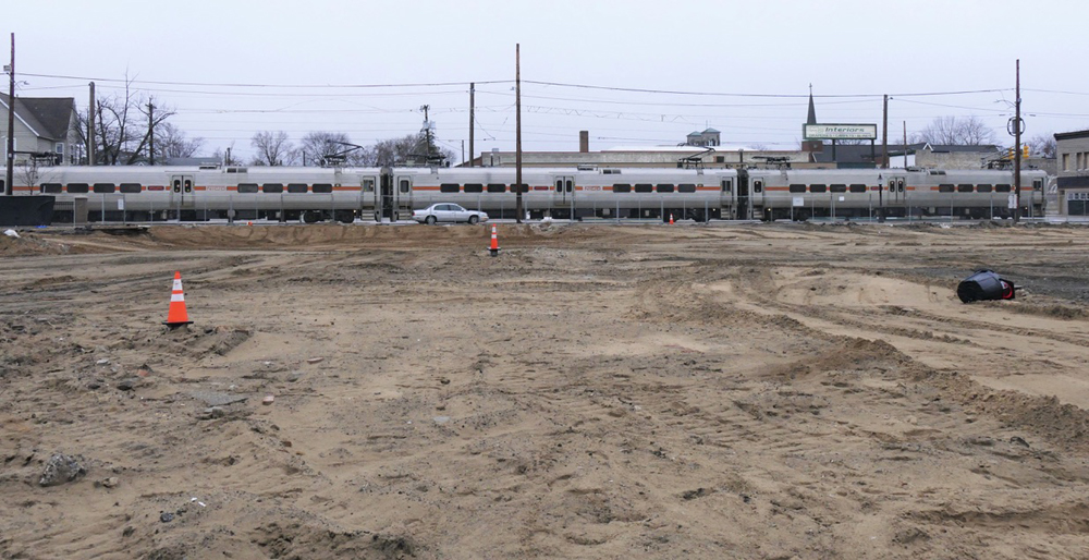 Commuter train passing lot of graded dirt