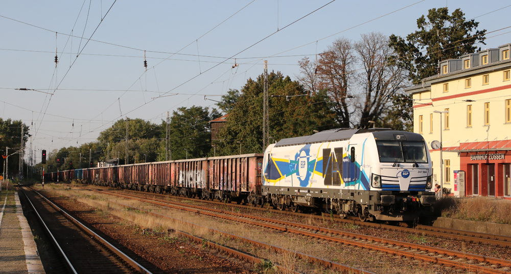 Train of hopper cars with electric locomotive passes station