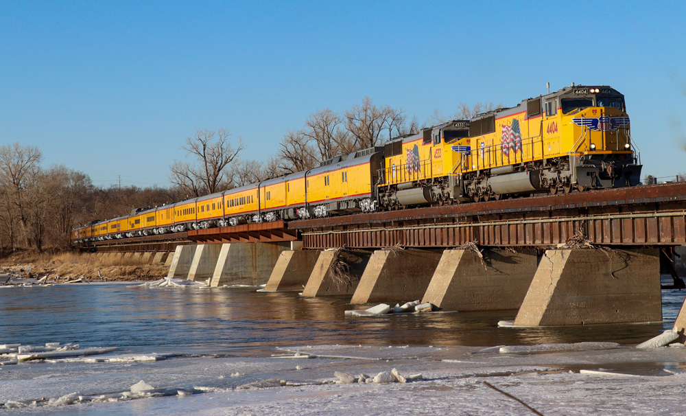 Passenger train with two locomotives and yellow cars on bridge