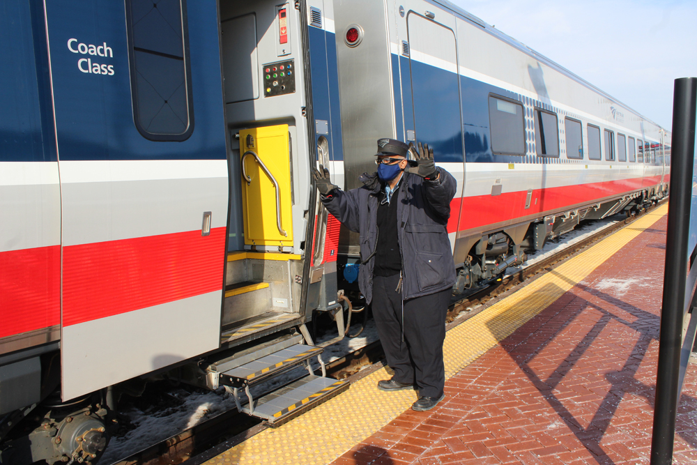 Conductor waves as he boards passenger car at platform