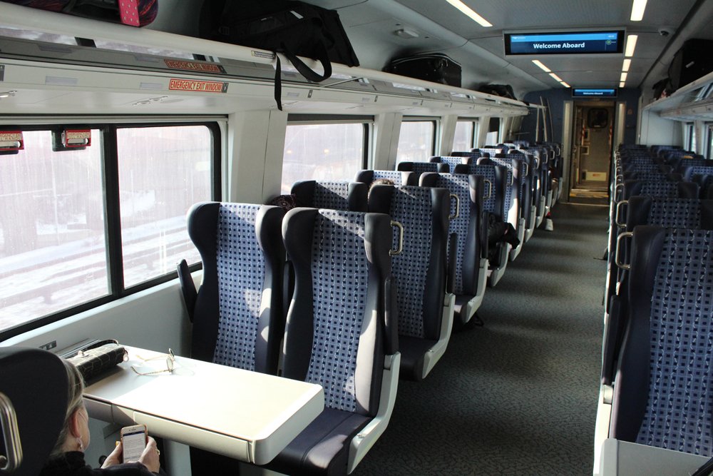 Interior of pasenger car with blue seats and a table in front of row nearest camera