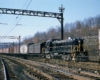 Black diesel locomotive pulls freight trains through junction under catenary wires
