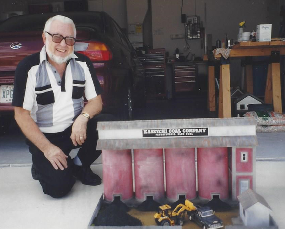 a man kneeling next to a model coal company building