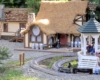 Model house with thatched roof next to gazebo.