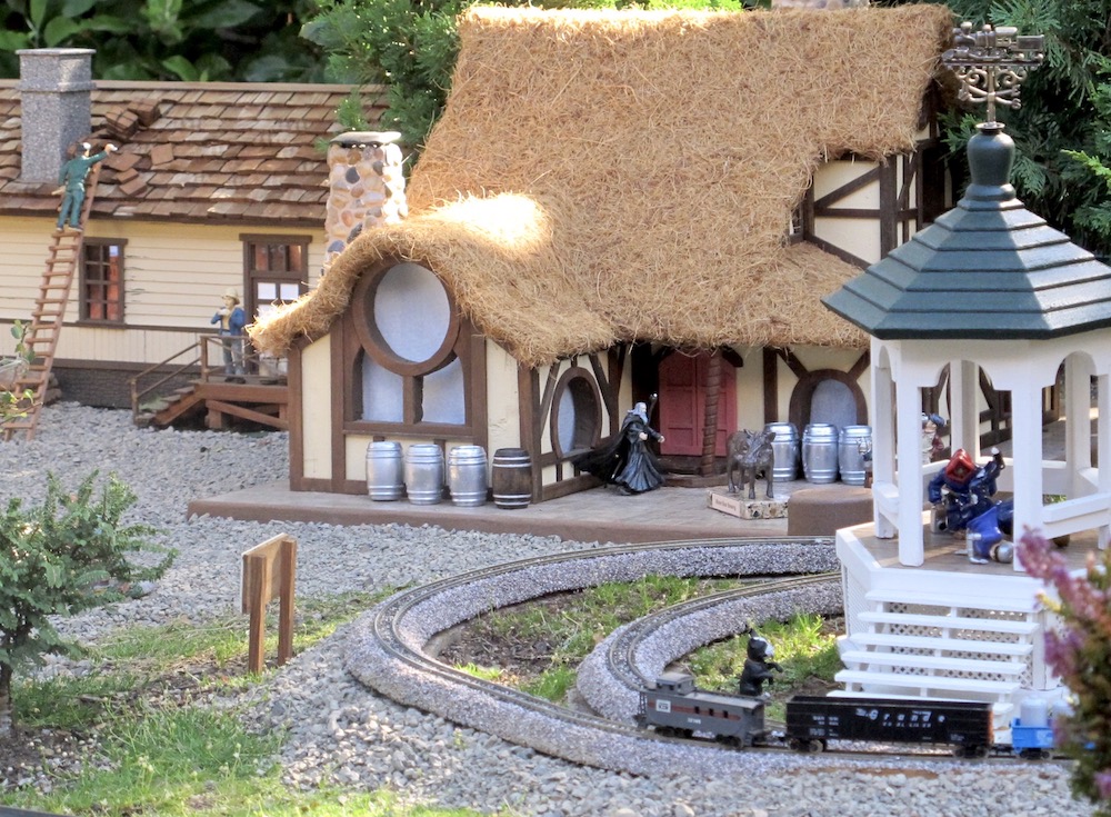 Model house with thatched roof next to gazebo.