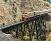 A gold-and-silver hood unit leads a passenger train onto a high steel trestle.