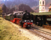 A black European steam locomotive pulls a string of green passenger cars up to the Niedlingen station.