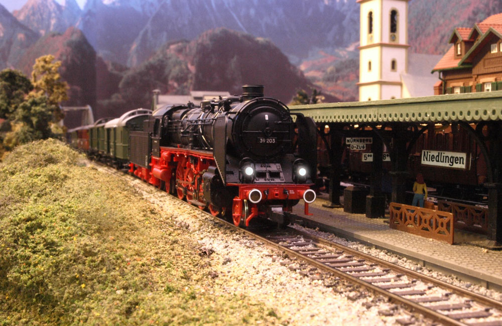 A black European steam locomotive pulls a string of green passenger cars up to the Niedlingen station.