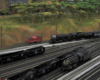 A black steam engine leads a mail train around the outskirts of a classification yard.