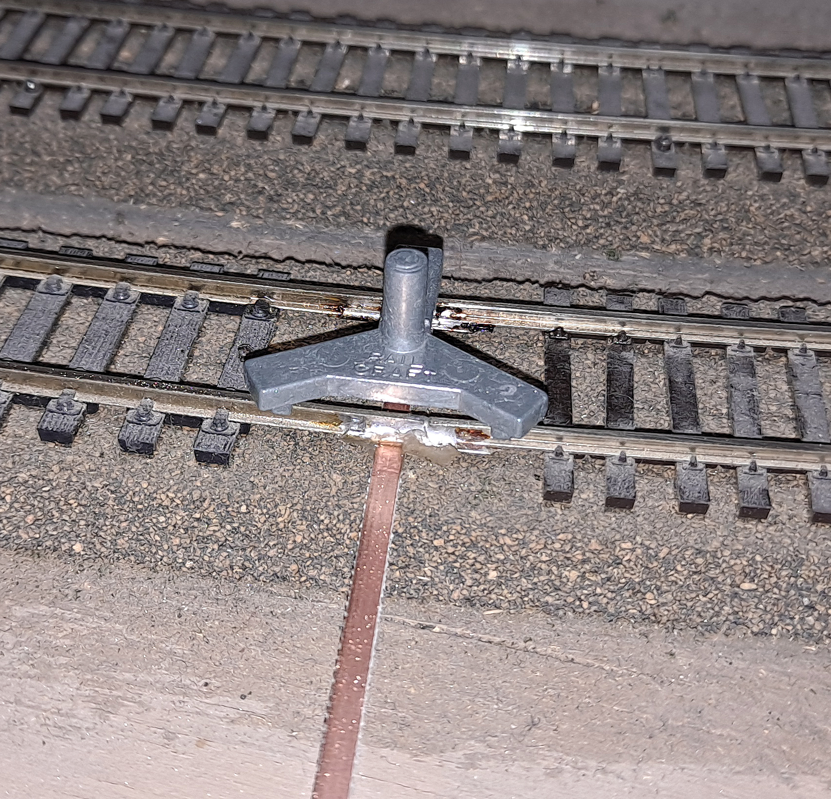 A three-point die-cast metal rail gauge sits above the rail joint.