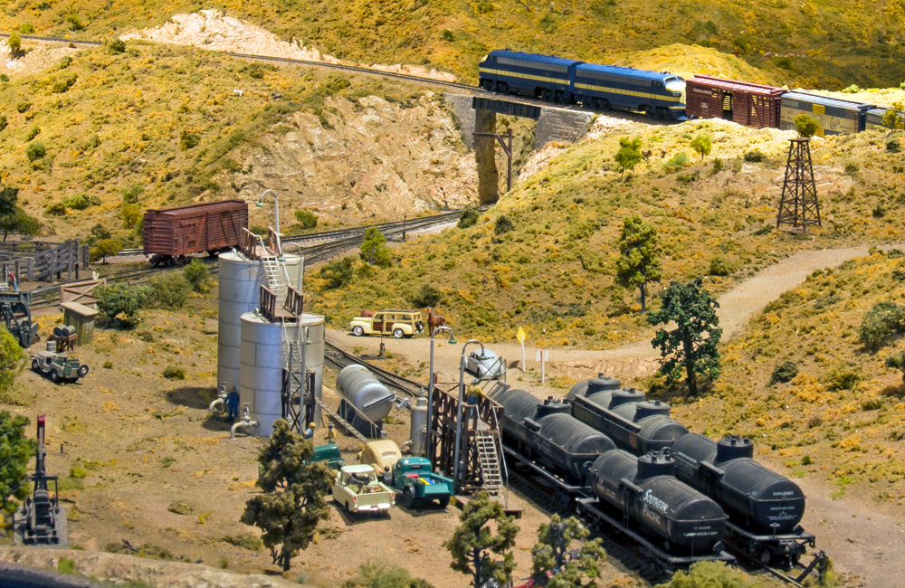 An HO scale scene of tank cars spotted at a loading rack, with storage tanks and an oil well nearby.