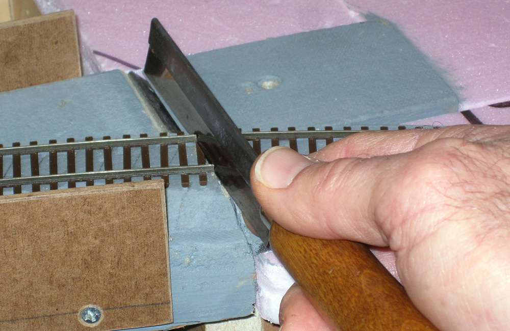 A razor saw cuts track glued down to blue expanded-foam insulation board.