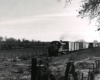 Back-lit black and white stripped locomotive leads freight train through arid landscape.