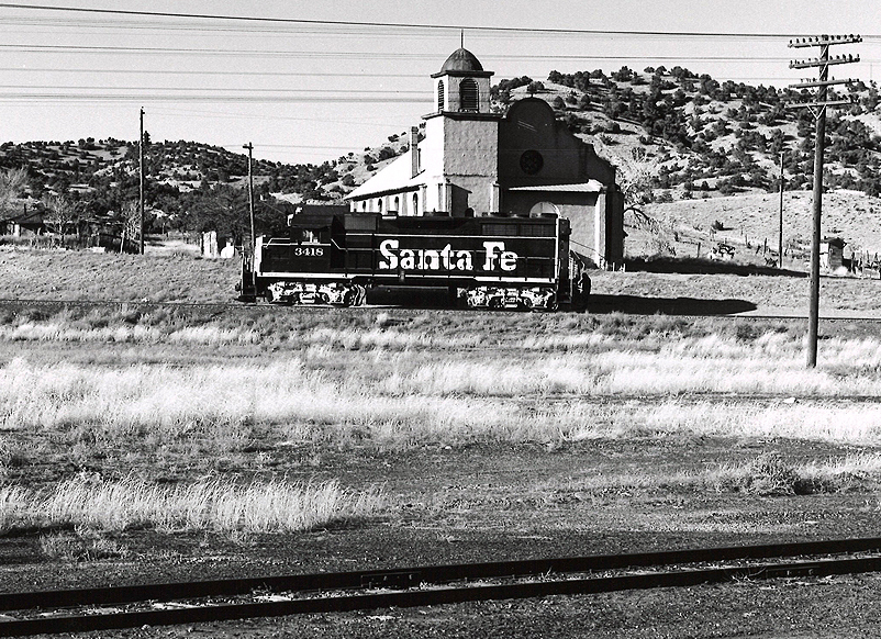 A lone diesel locomotive pauses in an arid landscaped rail yard.