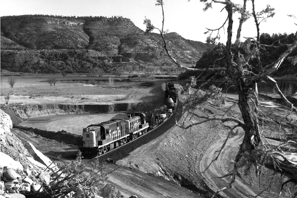 Short freight train winding through a wide river valley.