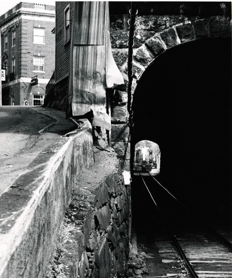 Artistic black and white image showing a train in a tunnel under a town.