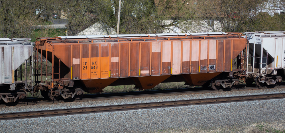 Photo of weathered orange covered hopper with light and dark orange patches and black lettering. 