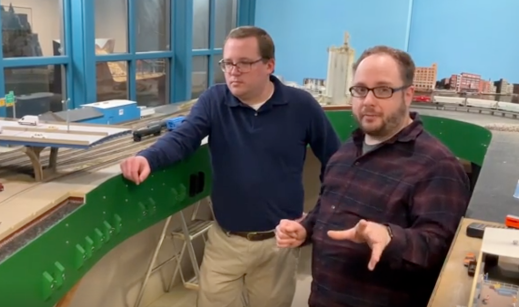 Two men in front of a model train layout.