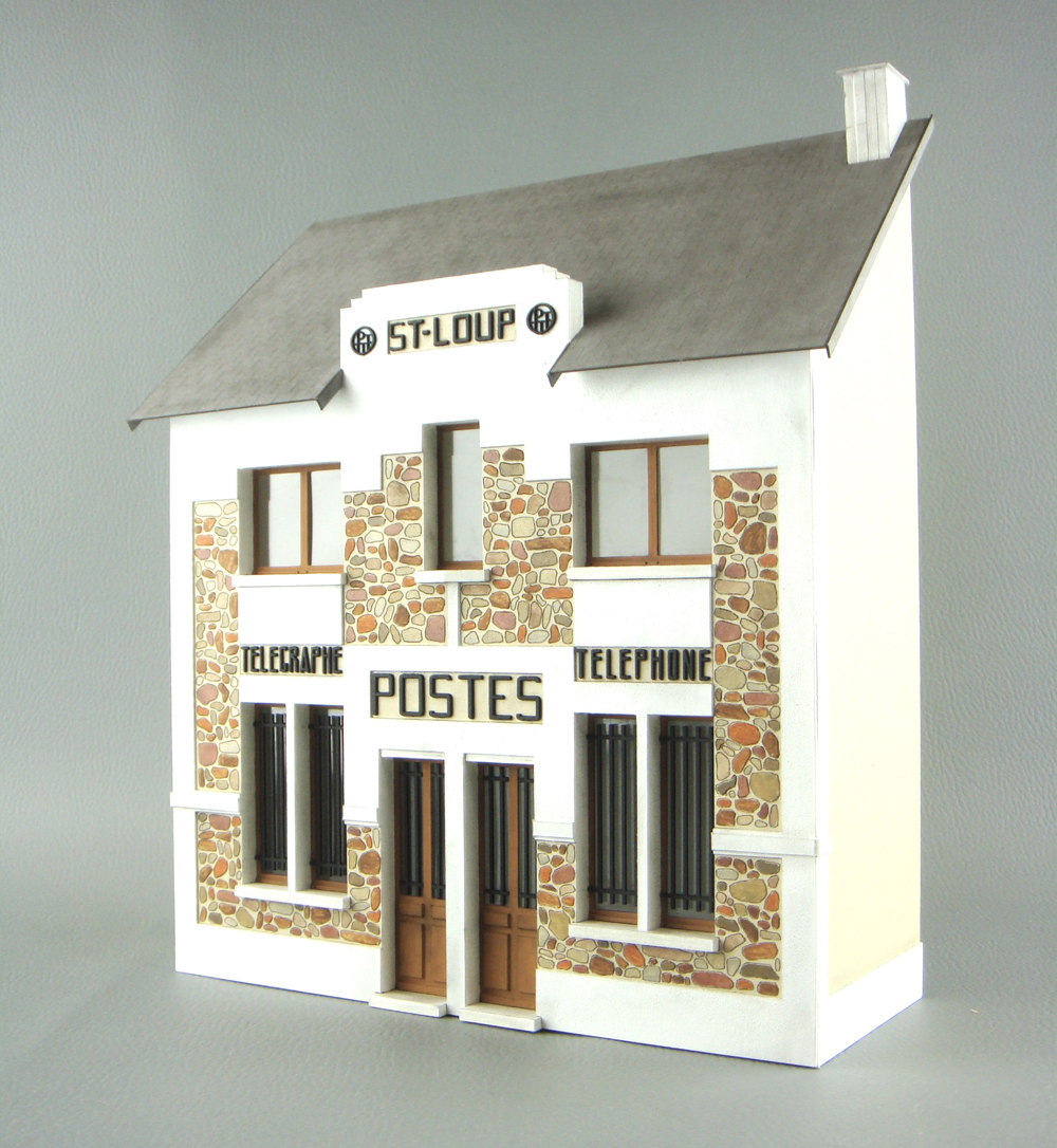 Photo of O scale low-relief structure kit painted white with gray roof, stone panels, and black lettering on gray background.