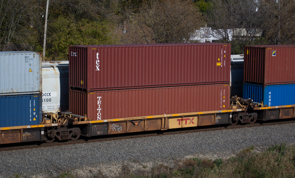 Photograph of grimy yellow well car with bright yellow patch and two oxide red containers inside.