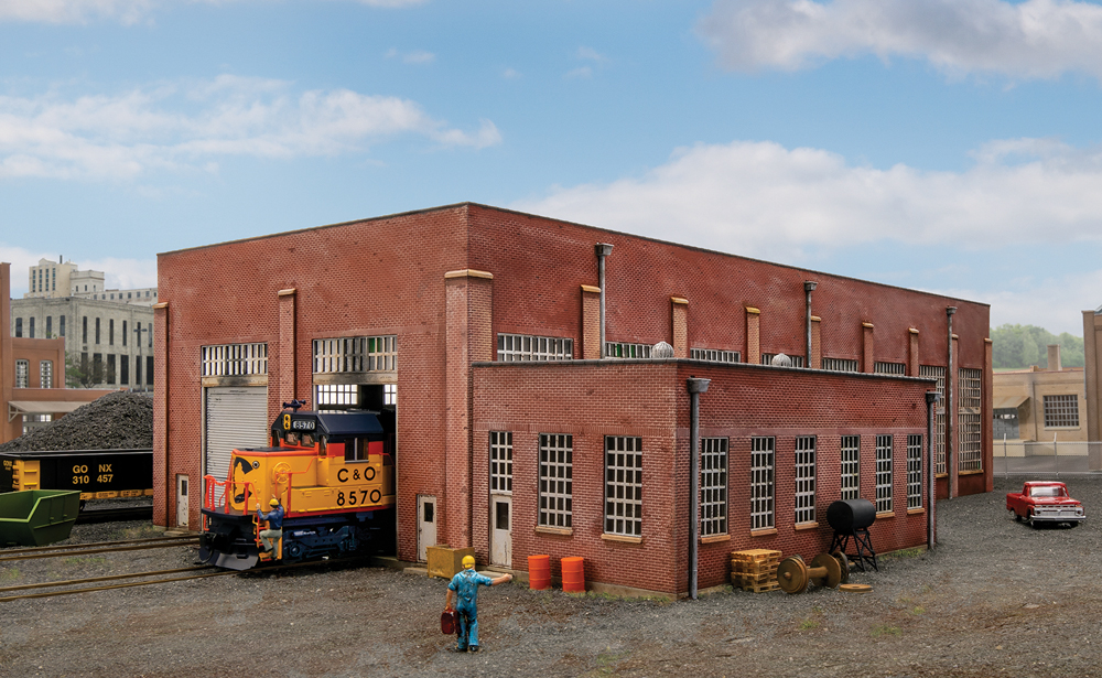 Photo of HO scale brick two-stall enginehouse in finished scene with locomotive, gondola, pickup truck, details, and photo backdrop.