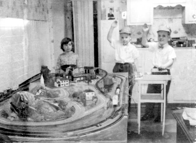 Black and white photo of three children next to a model train layout